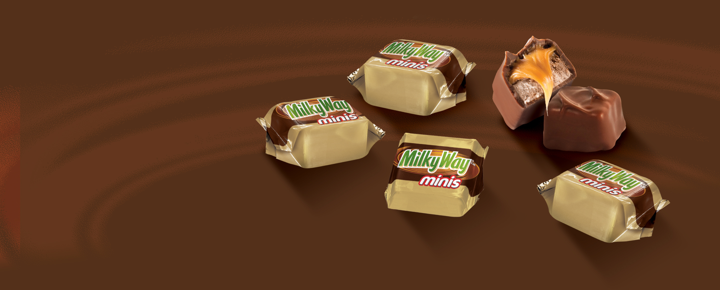Four packaged and one opened Milkyway mini chocolate bars on brown background